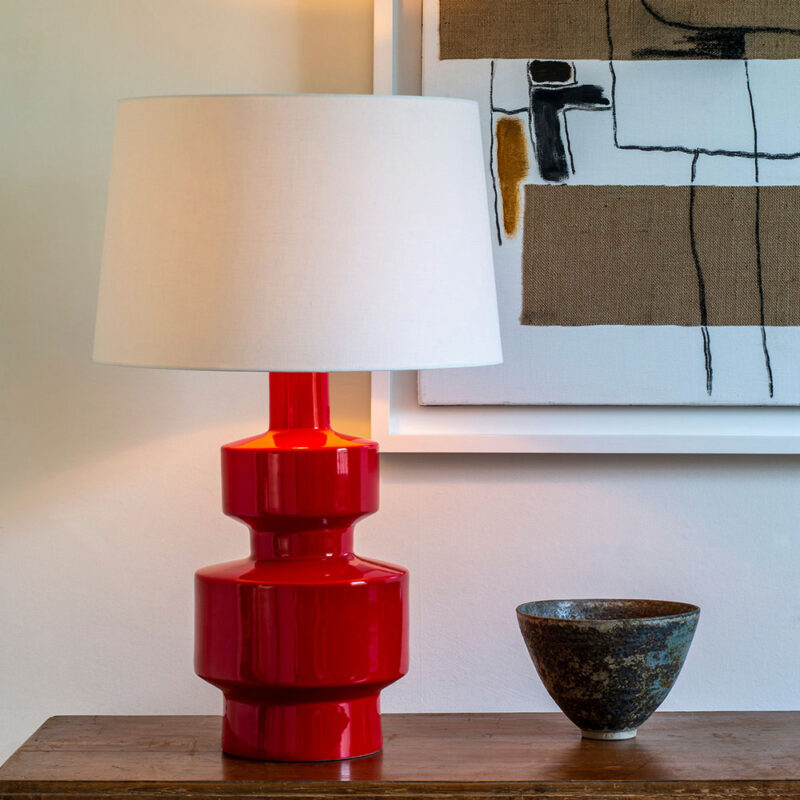 Miljøbilde av bordlampe med rød geometrisk lampefot og hvit skjerm i lin