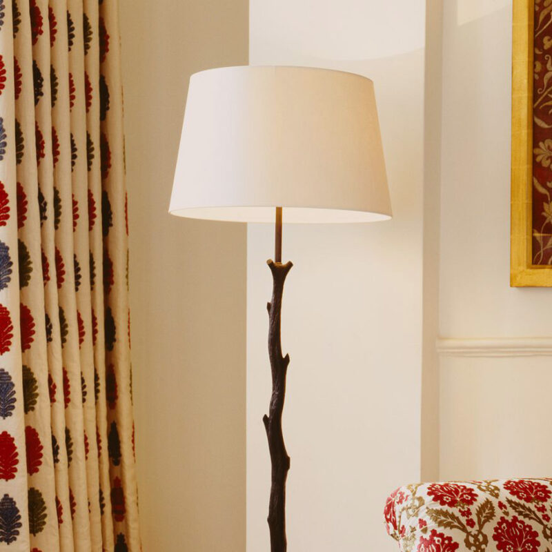 Miljøbilde av gulvlampe med fot i sort metall som kan se ut som en kvist, og med hvit klassisk lampeskjerm