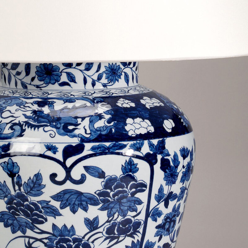Detaljbilde av bordlampe i blå og hvit i glasert keramikk med lys lampeskjerm.